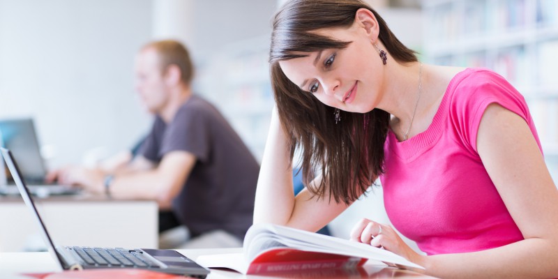 In the library – pretty female student with laptop and books